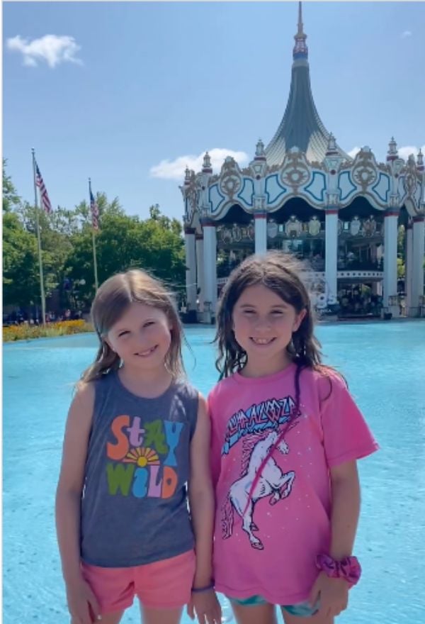 Girls standing in front of water with merry go round in background