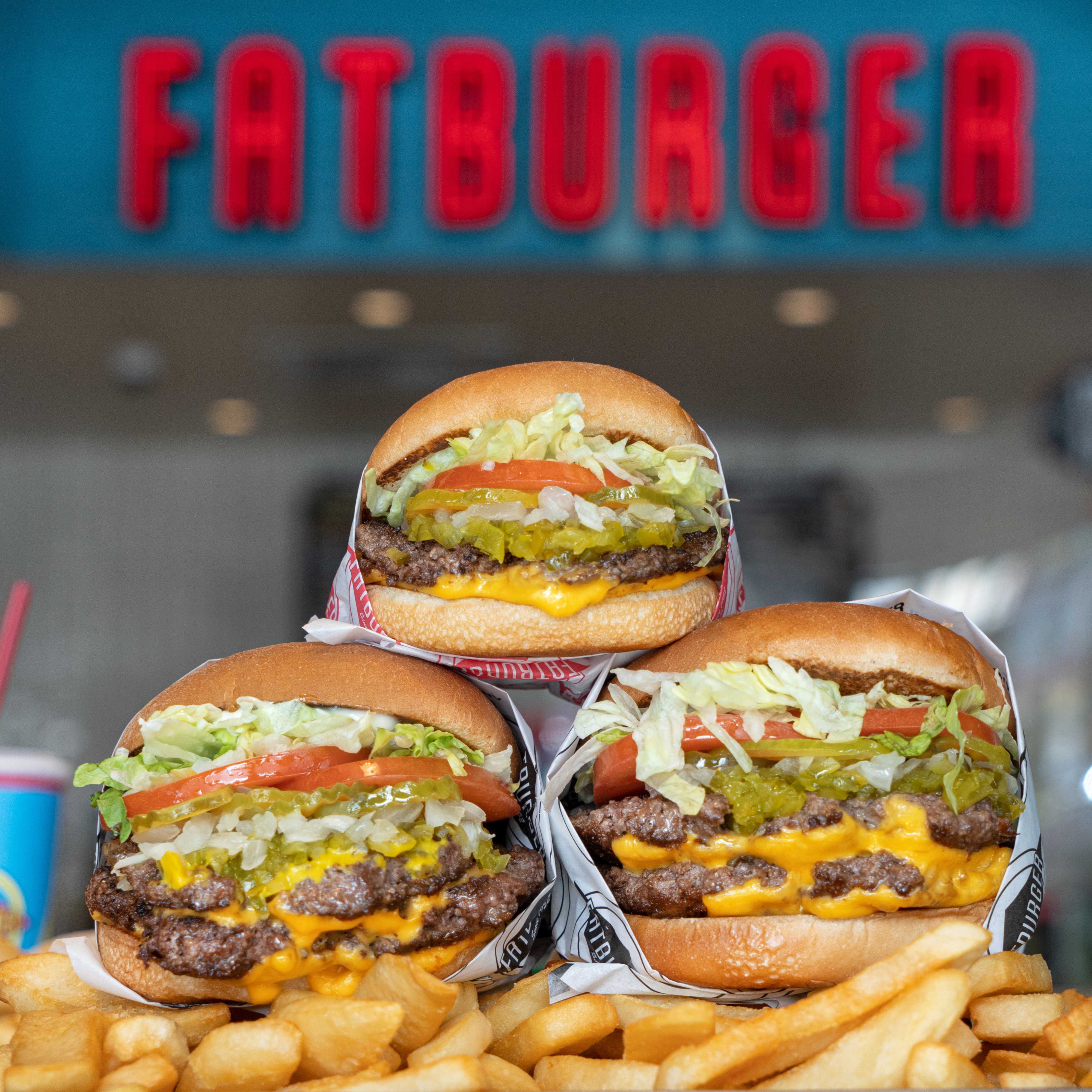 Stack of  burgers on top of fries in front of a Fatburger sign