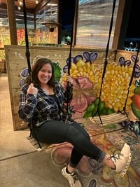 on a swing in plaid shirt, jeans, sticking legs out