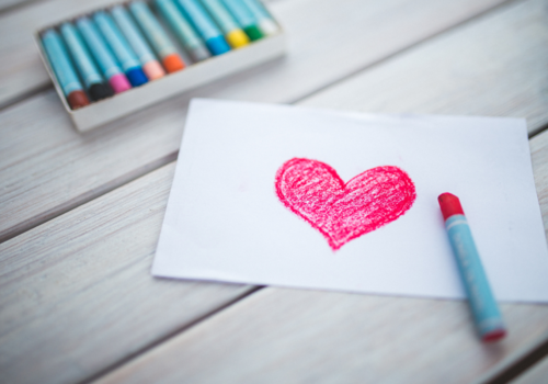 Paper, Heart Drawn in Pink Crayon, Pack of Crayons next to Paper