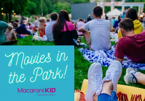 Shows families sitting on blankets in the grass waiting for an outdoor movie to start.