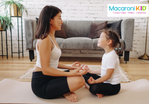 Parent and child sitting on the floor with cross legs, hands on knees -meditating at home