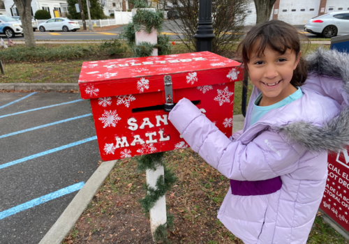 girl smiling as she puts her letter in Santa's mailbox