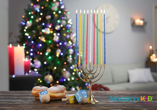A Menorah and Hanukkah treats on a table with a lit Christmas tree in the background