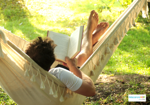 man laying in a hammock outside and reading a book