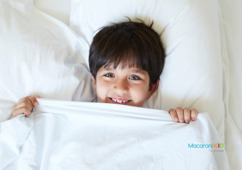 smiling child in bed with sheet pulled up to chin