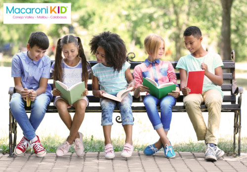 group of kids sitting on a bench outdoors and reading
