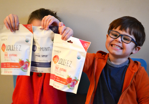 Two young children holding up bags of Lolleez Organic Throat Soothing Pops for Kids and Immuniteez Organic Immune Support* Pops