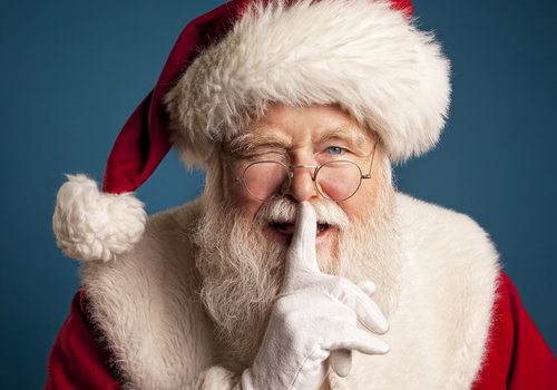 Santa winking at camera with finger over mouth to hush