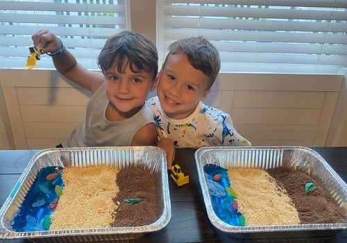 two boys with an edible sensory bin made to look like a beach with Jell-O, crushed cookies