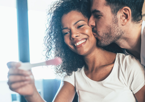 Smiling woman holding pregnancy test being kissed by man