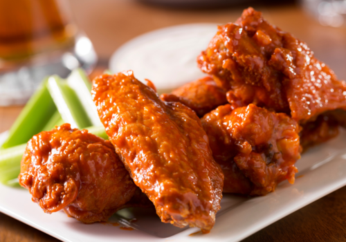 Photo of buffalo wings, celery, and dip on a white plate