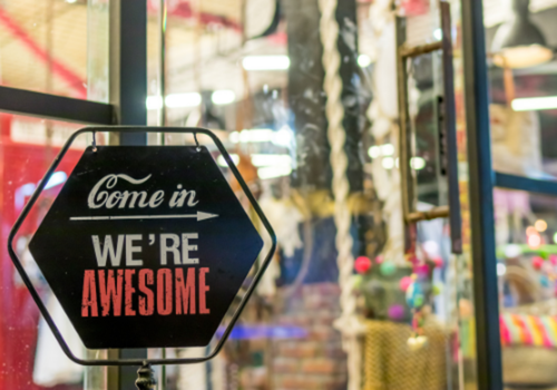 A sign on a store window that says come in we're awesome