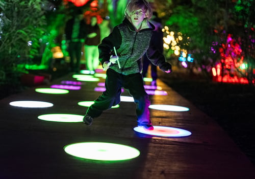 Elementary school aged child hoping on one foot on light patterns illuminated on the ground while their surroundings are dark.