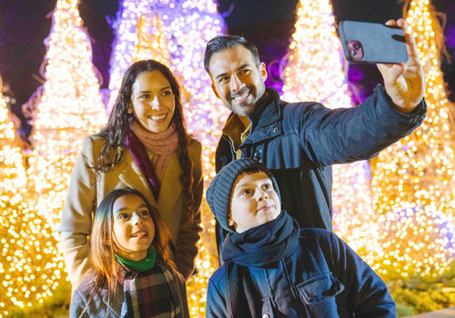 Family in front of Holiday glowing lights taking a selfie