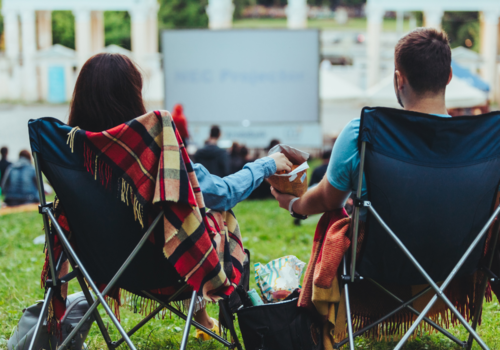 couple sitting in camp-chairs in city park looking movie outdoors at open air cinema