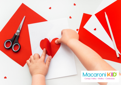 Child making a Valentine's Day card using red and white paper and a scissors