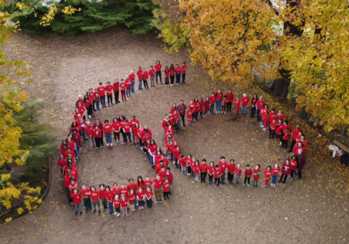 An aerial photo of people standing in the shape of the number 60. Autumn looking trees nearby.