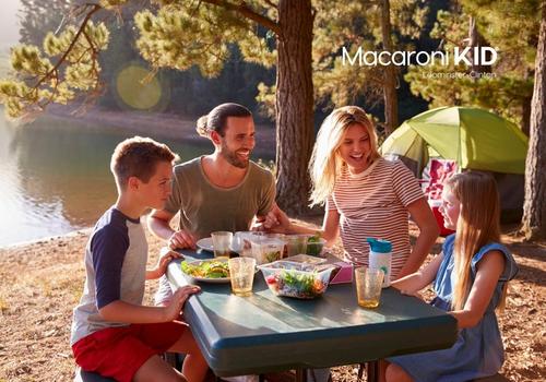 Two adults and two young kids eating at a picnic table at campsite next to a pond.