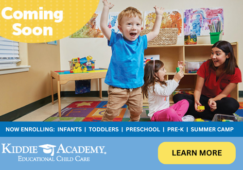 A child sitting on a rug with a female adult and another child standing with hands in air and happy face.  Early childhood center as the background.