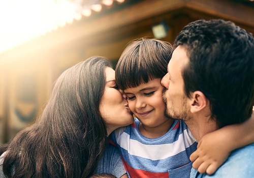 two parents kissing son on cheeks