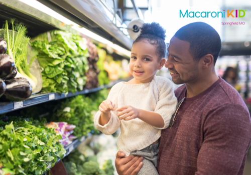 a little girl and her dad are shopping in the grocery store and looking at lettuce, spinach, and eggplants in the produce department.