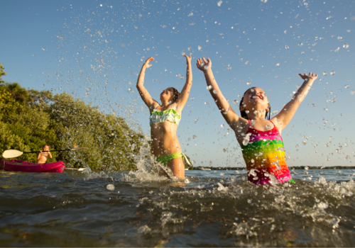 Two kids splashing in the lake and one on a kayak