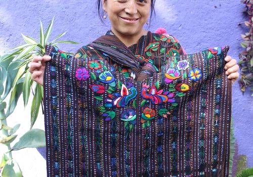 Candelaria- artisan from Guatemala holds a traditional Guatemalan blouse known as Tzoloj Ya’ huipil