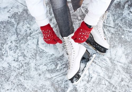 Ice skates on someone's feet. Red gloves on hands tying laces.