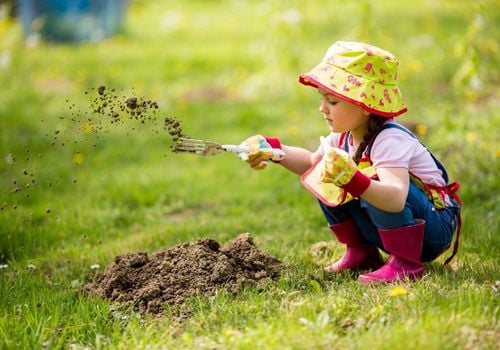 young child wearing a sun hat, gardening gloves, digging in dirt