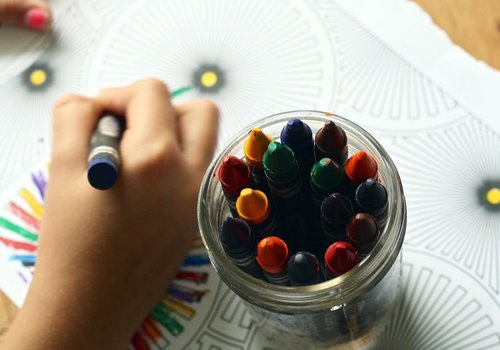 Child hand colouring with a jar of crayons