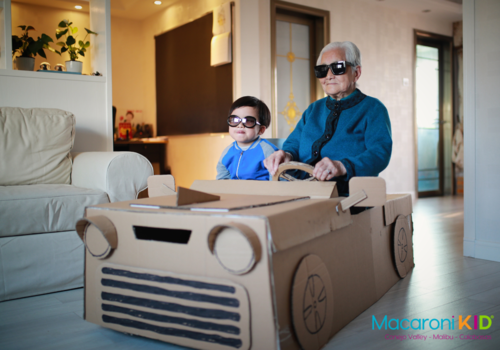 little boy and grandparent sitting in a cardboard car watching 3D movie