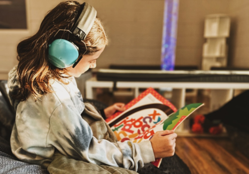 sensory sensitive child looking at a book while wearing noise-cancelling headphones