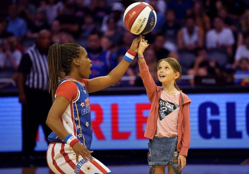 Harlem Globetrotters team member spinning a basketball on a childs finger on the court.