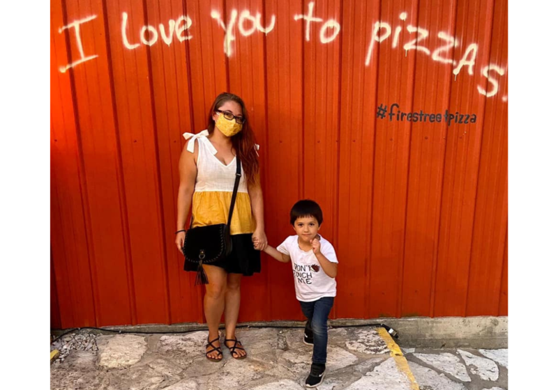 Brittany and son stand in front a red wall at Fire Street Pizza that says I love you to pizzas.