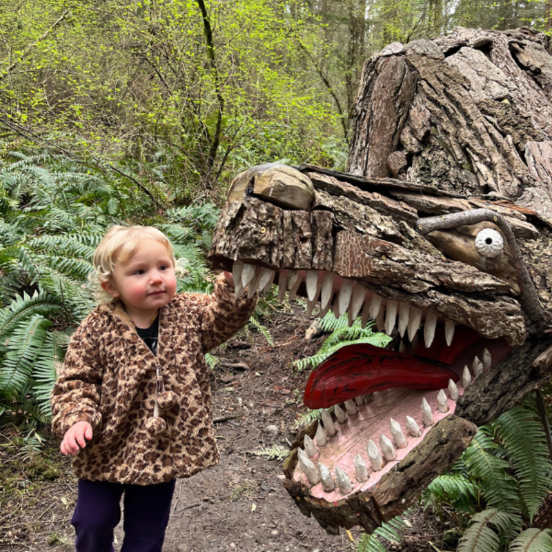 Toddler petting a dinosaur wooden sculpture