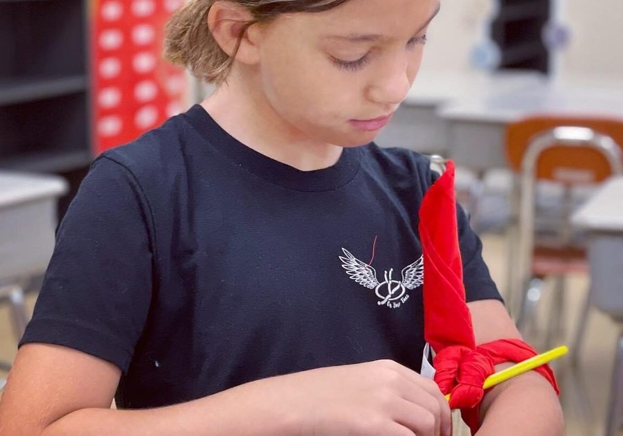 Young child wrapping a pretend bandage around his arm ins Little Medical School's Wilderness Medicine School