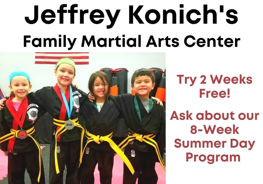 4 young kids dressed in black karate uniforms smiling in class.