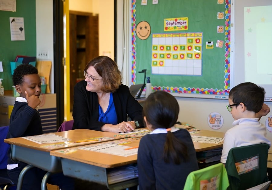 teacher sitting at desk with three students