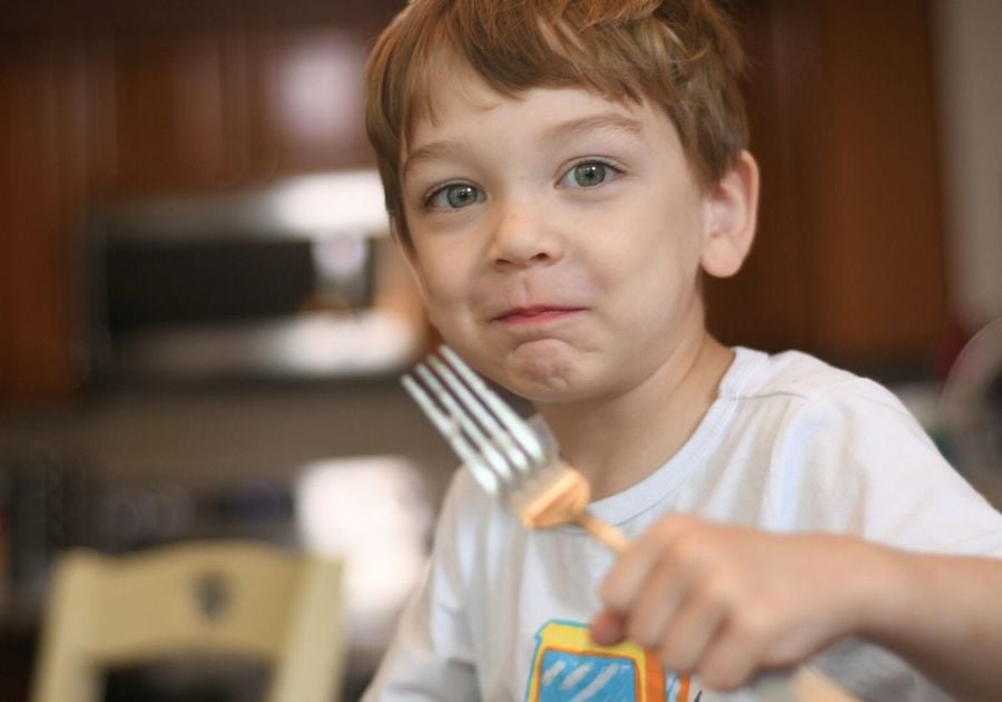 Child eating chicken adobo at the dinner table with a mouth full of food grinning happy enjoying his meal