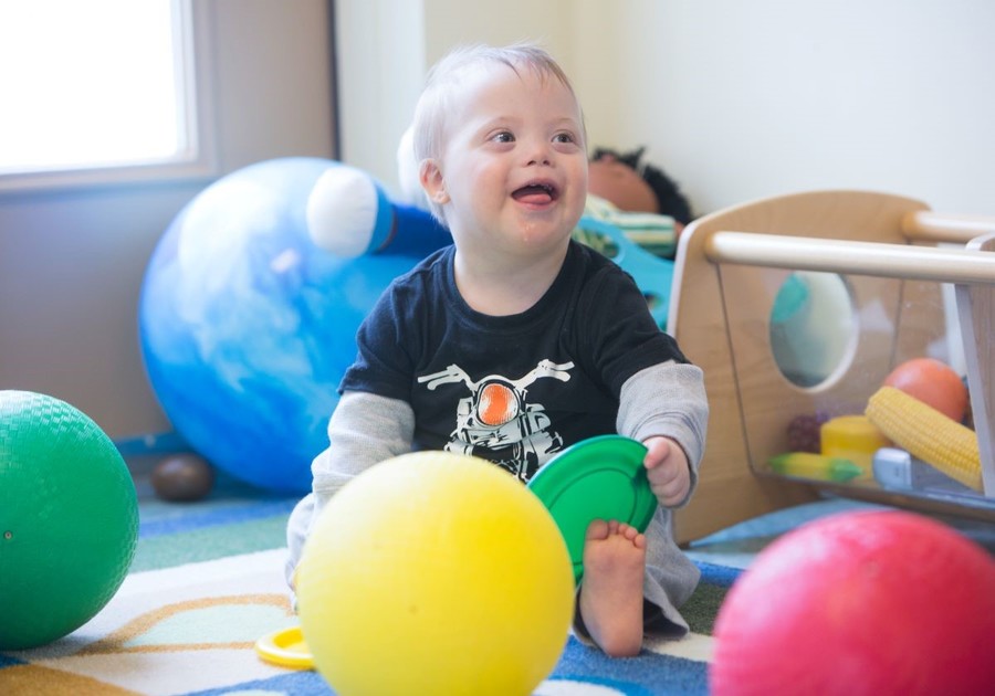 baby with down syndrome playing with yellow ball