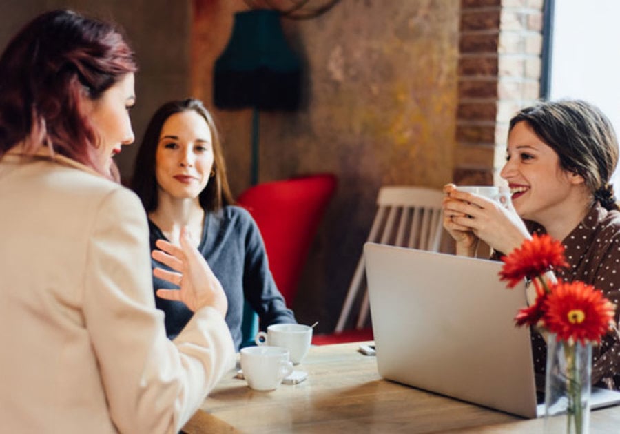 three women sitting around table with laptop and coffee