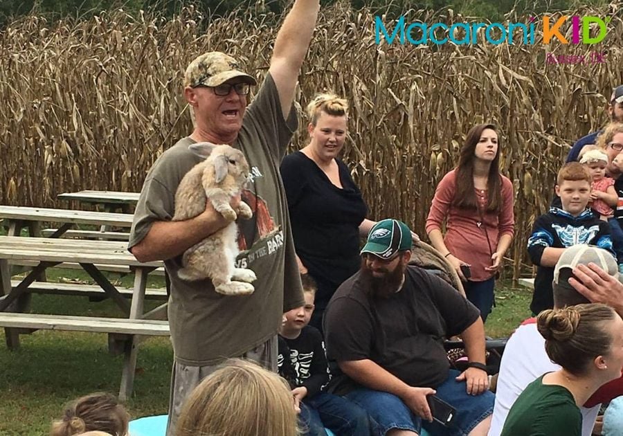 Group of people sitting at farm. Farmer is holding a rabbit.