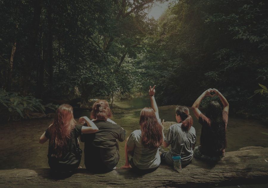 view of the backs of 5 women sitting on a log over looking a creek