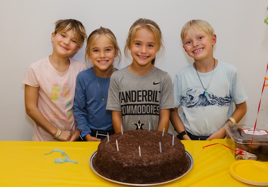 four kids behind a birthday cake