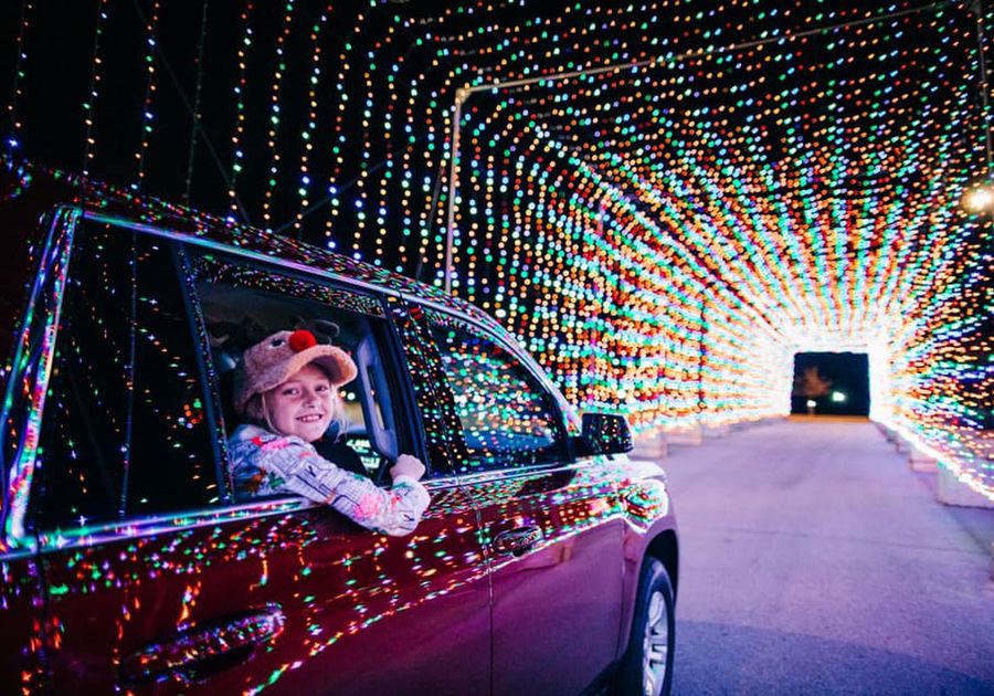 Kid smiling at camera from back seat of car while driving through holiday light tunnel