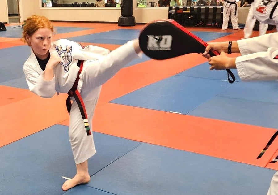 girl in karate uniform kicking mat