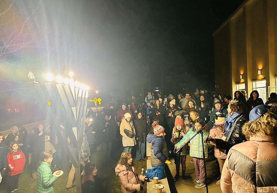 Crowd of people listening to a performer; Menorah lit.