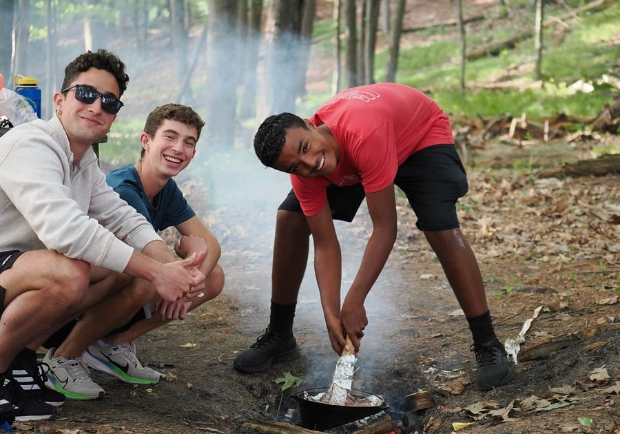 three teens cooking over a fire