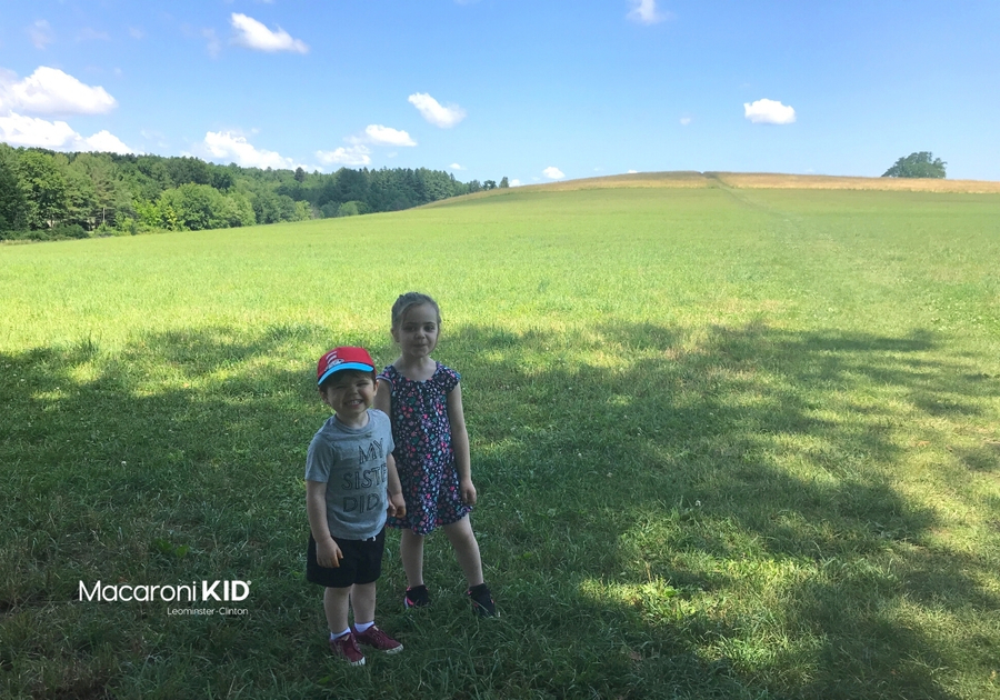 Two young children standing in the shade at the bottom of a large grassy hill.